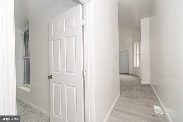 hallway with visible vents, light wood-style flooring, and baseboards