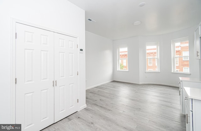 unfurnished bedroom with visible vents, a closet, light wood-style flooring, and baseboards