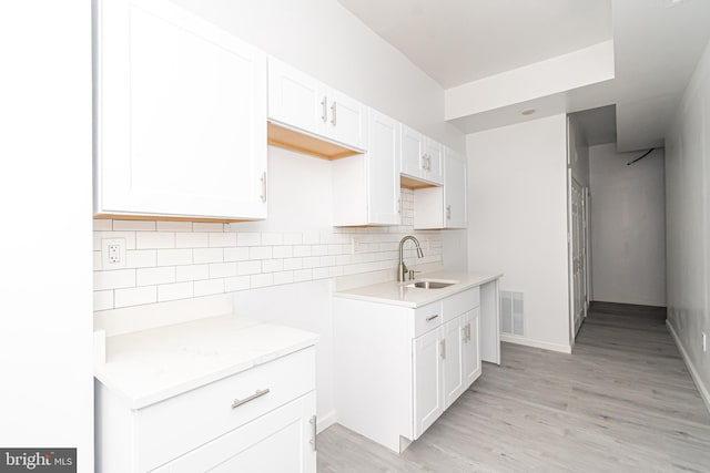 kitchen with visible vents, light wood-style flooring, decorative backsplash, white cabinetry, and a sink