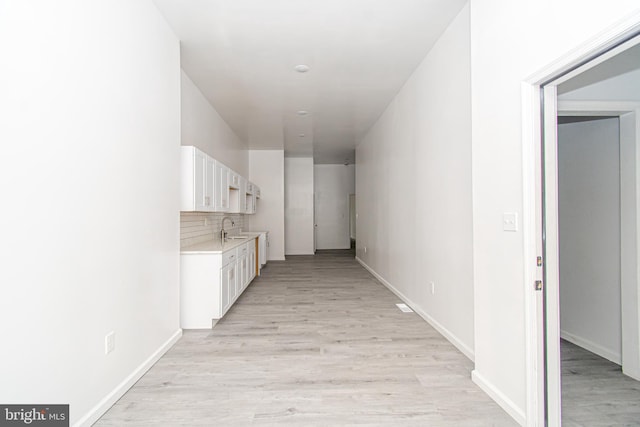 corridor featuring light wood finished floors, a sink, and baseboards