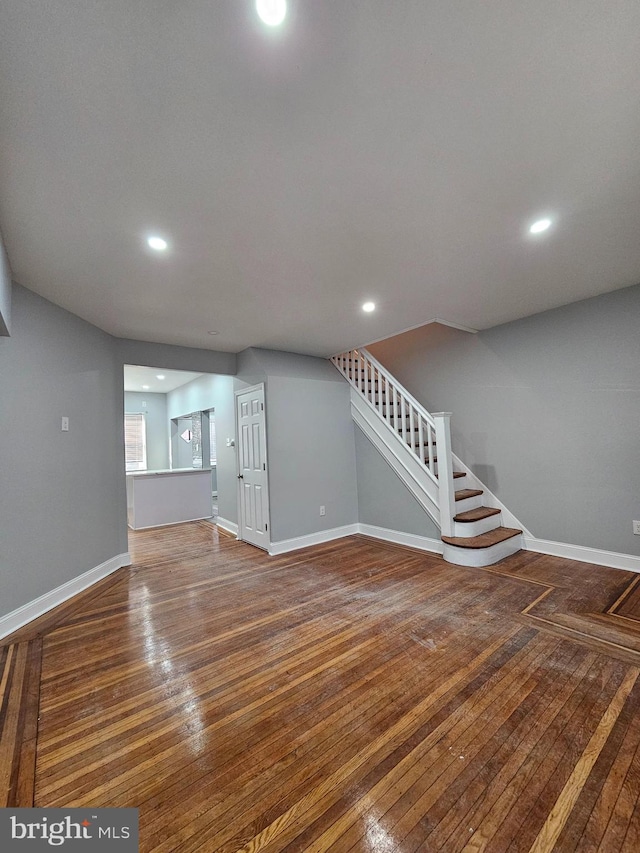 unfurnished living room featuring recessed lighting, wood-type flooring, baseboards, and stairs