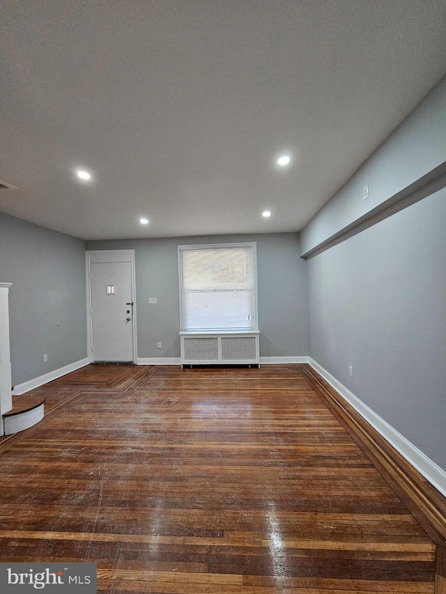 empty room featuring dark wood-type flooring, baseboards, and radiator heating unit