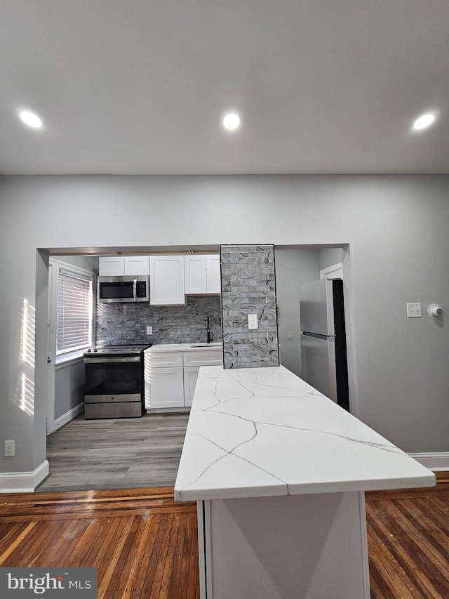 kitchen featuring dark wood-style floors, light stone counters, stainless steel appliances, white cabinetry, and a sink