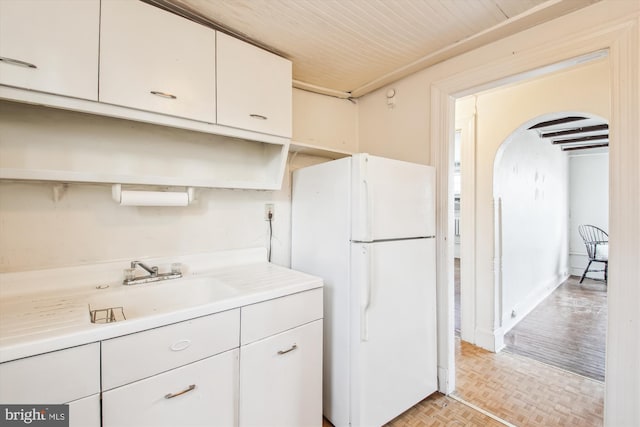 kitchen with arched walkways, white cabinets, freestanding refrigerator, light countertops, and a sink