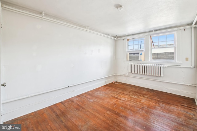 empty room with baseboards, wood-type flooring, and radiator