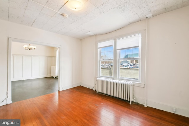 spare room featuring dark wood-style floors, radiator, baseboards, and an inviting chandelier