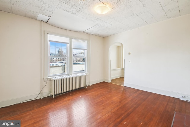 empty room with radiator, dark wood-style floors, baseboards, and arched walkways