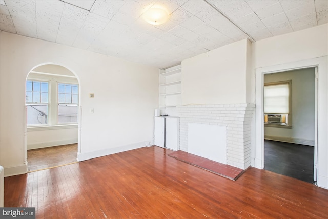 unfurnished living room with arched walkways, dark wood-style flooring, a fireplace, and baseboards