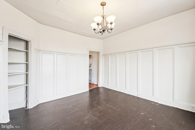 unfurnished bedroom with an inviting chandelier, a decorative wall, and dark wood-type flooring