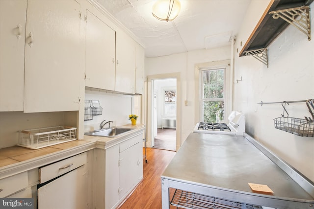 kitchen featuring white cabinets, radiator heating unit, light wood-style flooring, light countertops, and a sink