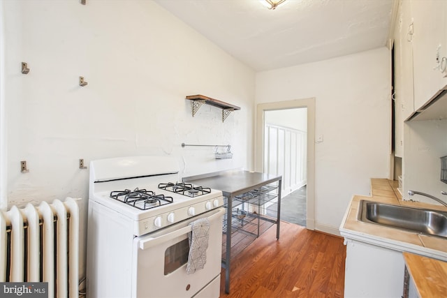 kitchen featuring radiator heating unit, wood finished floors, light countertops, open shelves, and gas range gas stove