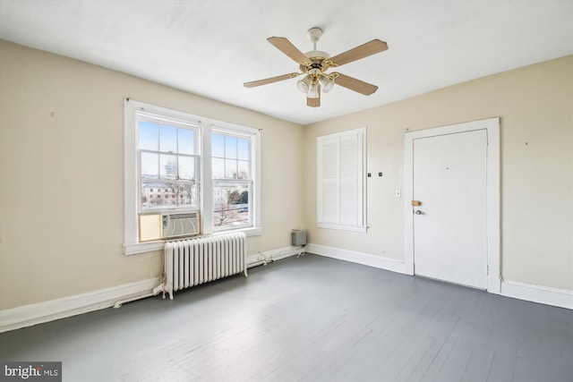 empty room featuring dark wood-style flooring, radiator heating unit, a ceiling fan, and baseboards