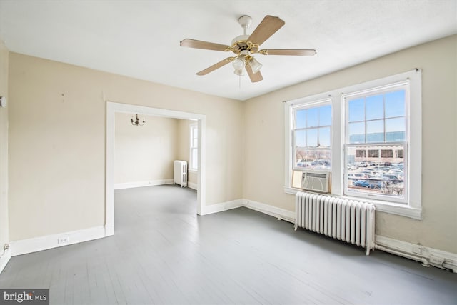 empty room with ceiling fan with notable chandelier, radiator, baseboards, and wood finished floors