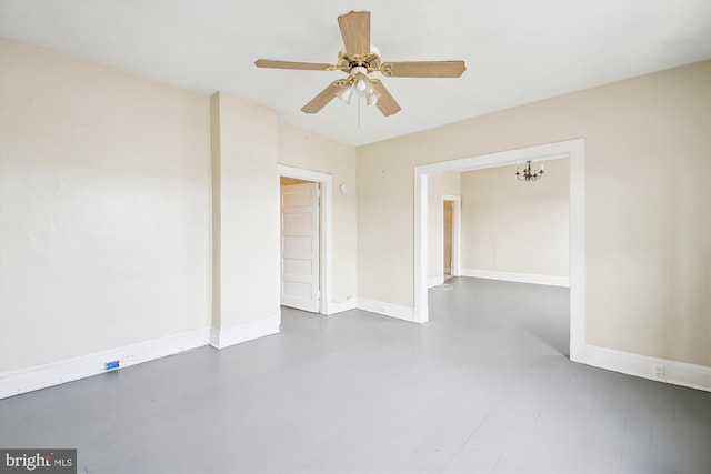 spare room featuring finished concrete floors, baseboards, and ceiling fan with notable chandelier