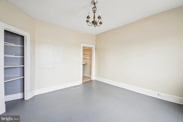 spare room with finished concrete flooring, baseboards, and a notable chandelier