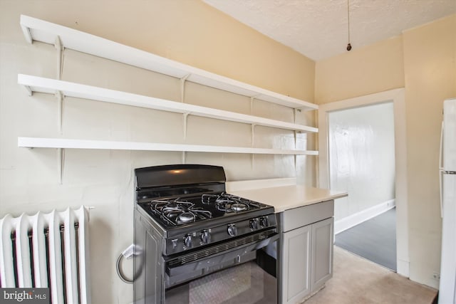 kitchen featuring radiator, light countertops, gray cabinetry, black gas stove, and open shelves