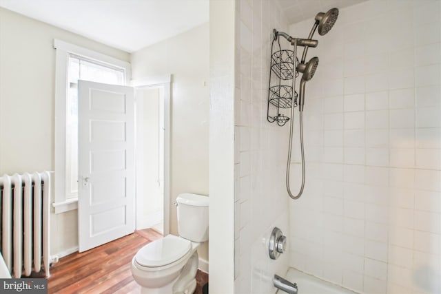 bathroom with toilet, wood finished floors, baseboards, shower / bathing tub combination, and radiator heating unit