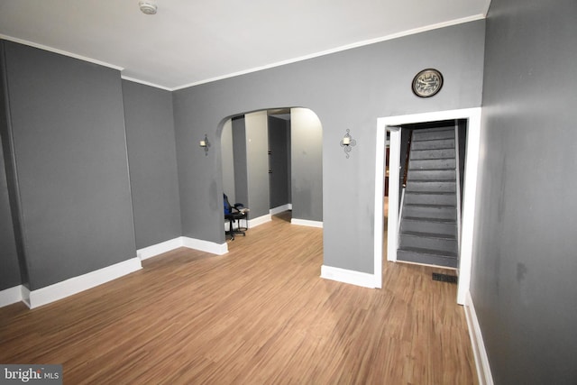 empty room with arched walkways, crown molding, light wood-style floors, baseboards, and stairs