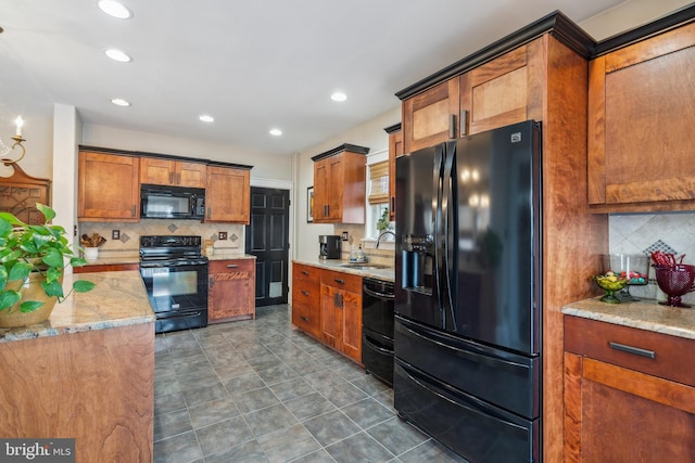 kitchen featuring light stone counters, brown cabinets, a sink, black appliances, and backsplash