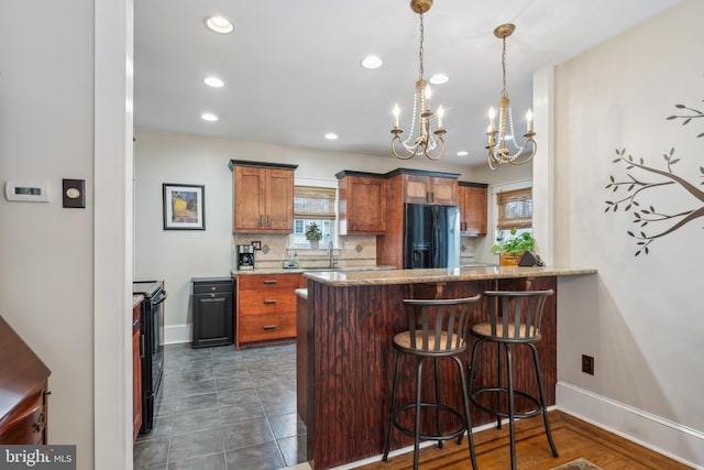 kitchen with a peninsula, a breakfast bar, a sink, backsplash, and black appliances