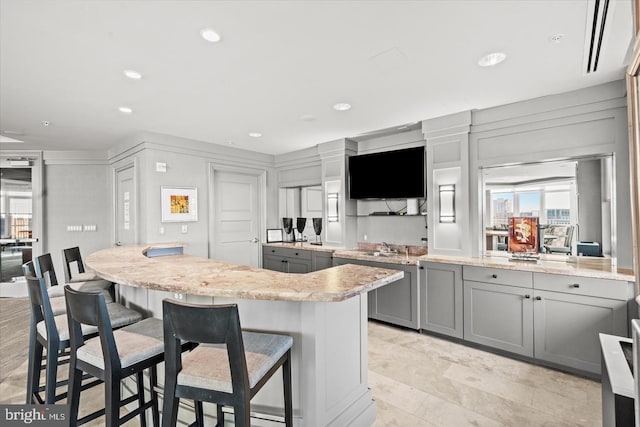 kitchen featuring recessed lighting, gray cabinets, a kitchen island, light stone countertops, and a kitchen bar