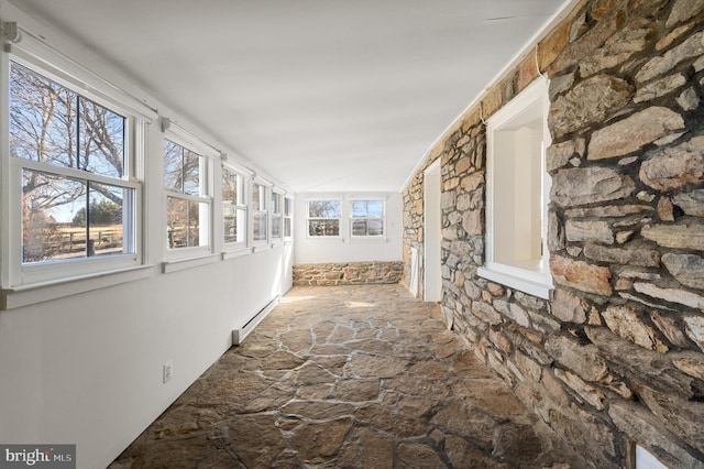 corridor with a baseboard heating unit, vaulted ceiling, and stone flooring