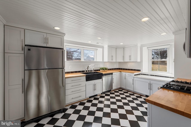 kitchen with dark floors, stainless steel appliances, wooden counters, white cabinetry, and a sink