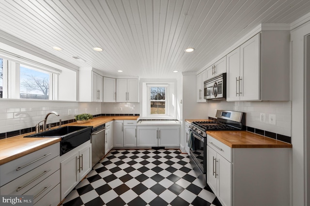 kitchen featuring butcher block counters, dark floors, appliances with stainless steel finishes, white cabinetry, and a sink