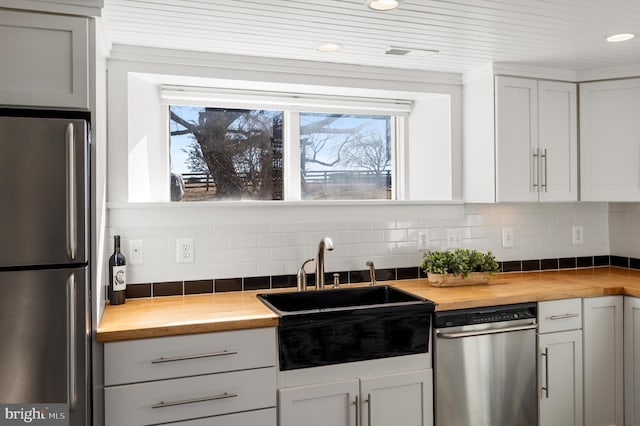 kitchen featuring butcher block counters, visible vents, decorative backsplash, appliances with stainless steel finishes, and a sink