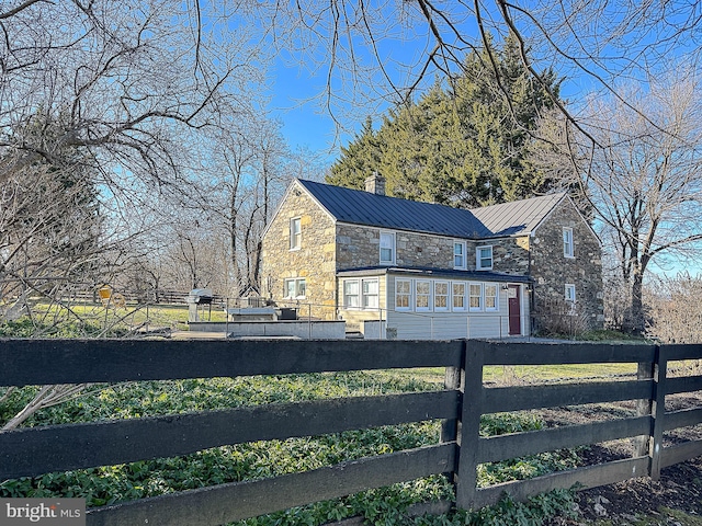 view of side of property with a standing seam roof, stone siding, fence, and metal roof