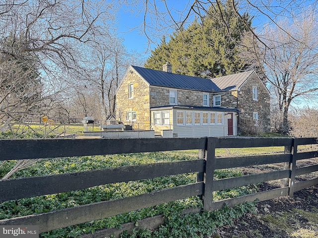 view of property exterior with stone siding, a standing seam roof, fence, and metal roof