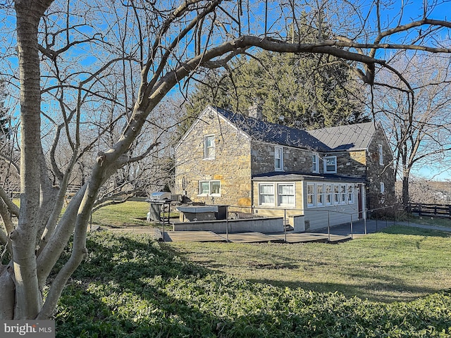 back of house with fence, a yard, stone siding, a patio area, and a hot tub