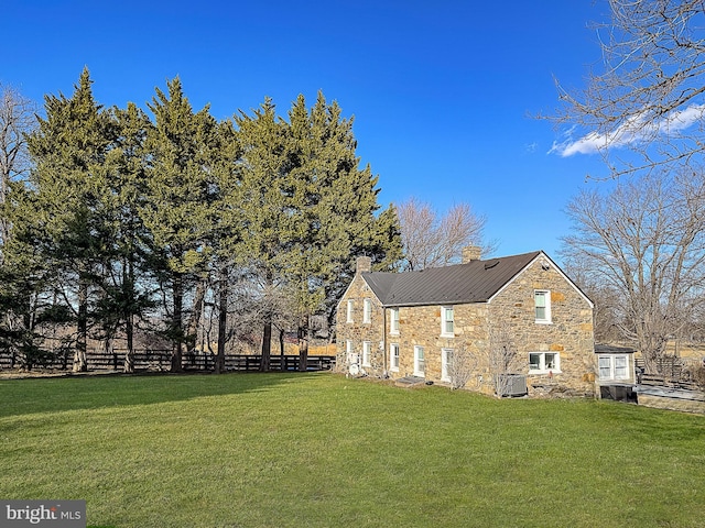 view of side of home with stone siding, a chimney, fence, and a lawn