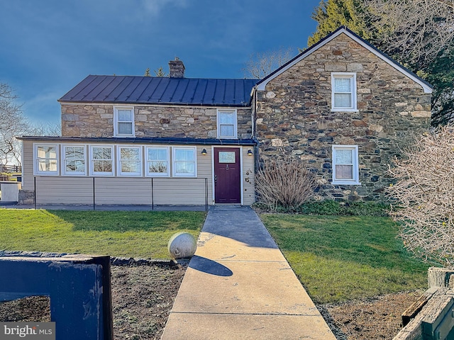 view of front of property with a standing seam roof, metal roof, a chimney, and a front lawn