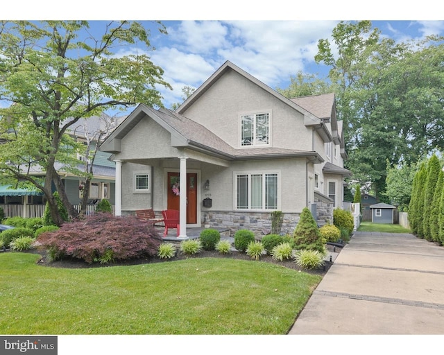 view of front facade featuring a storage unit, stucco siding, stone siding, an outdoor structure, and a front lawn