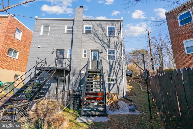 rear view of house with brick siding, a chimney, a patio area, fence, and stairs