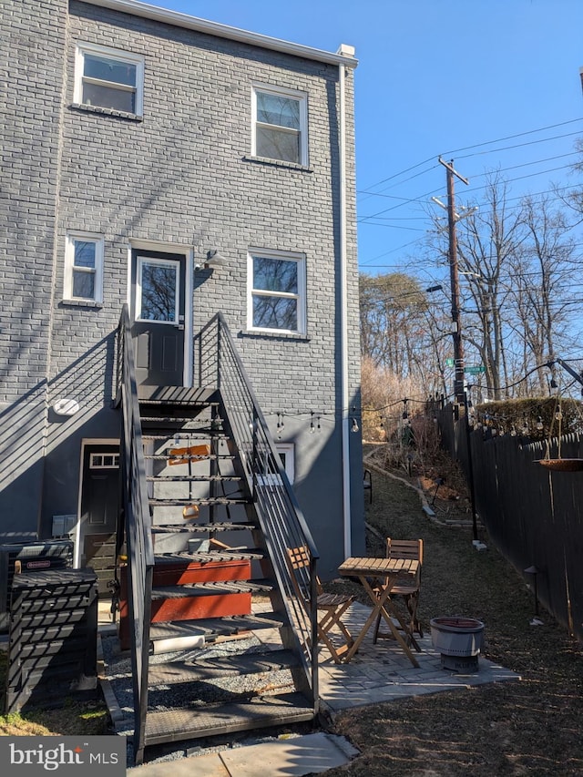 rear view of property with a fire pit, a patio, brick siding, and fence