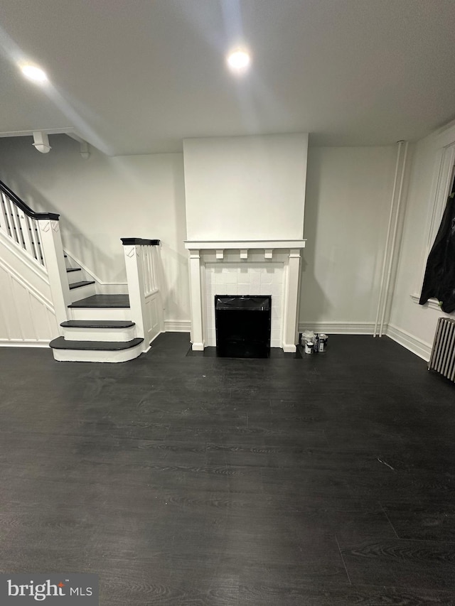 unfurnished living room with baseboards, dark wood finished floors, a tiled fireplace, radiator, and stairway