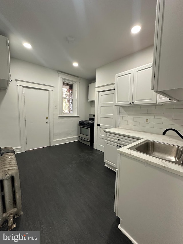 kitchen with stainless steel gas stove, dark wood finished floors, light countertops, white cabinetry, and a sink