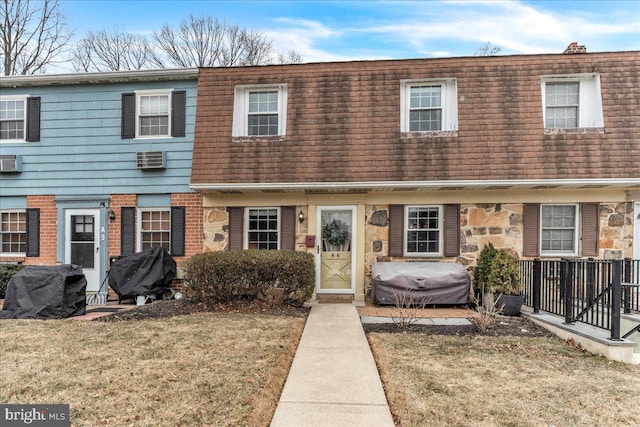 multi unit property with mansard roof, a front lawn, a shingled roof, and brick siding