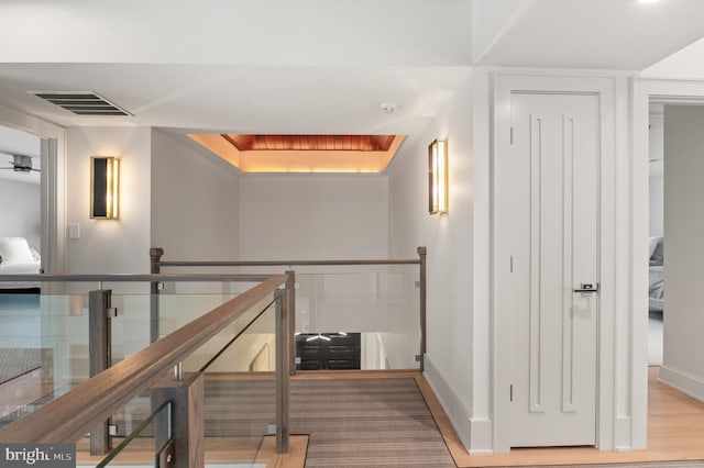 hallway with wood finished floors, an upstairs landing, visible vents, and baseboards