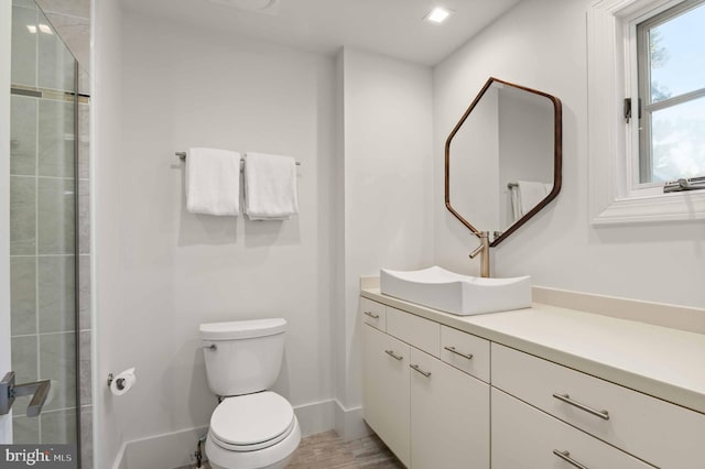 bathroom featuring a tile shower, toilet, vanity, and baseboards