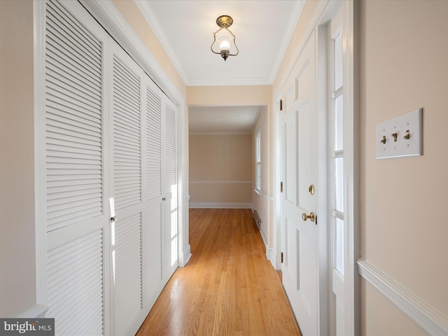 hall featuring light wood-style floors, baseboards, ornamental molding, and a wealth of natural light