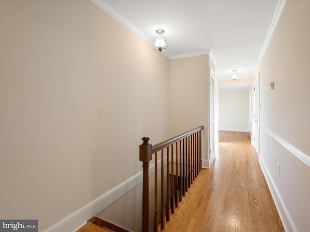 hallway with light wood-style floors, baseboards, ornamental molding, and an upstairs landing