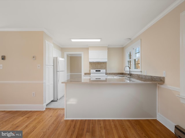 kitchen with a peninsula, white appliances, white cabinets, and a sink