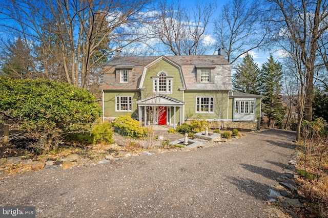 view of front of home featuring driveway, a chimney, and a gambrel roof