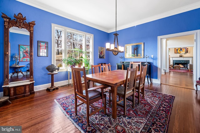 dining room with hardwood / wood-style flooring, a fireplace, baseboards, ornamental molding, and an inviting chandelier