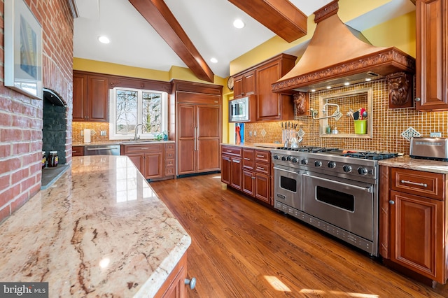 kitchen with built in appliances, premium range hood, beamed ceiling, and light stone counters