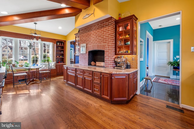 kitchen with decorative light fixtures, wood finished floors, lofted ceiling with beams, glass insert cabinets, and light stone countertops