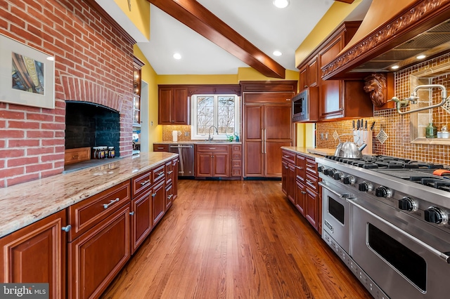 kitchen featuring decorative backsplash, light stone counters, wood finished floors, built in appliances, and premium range hood